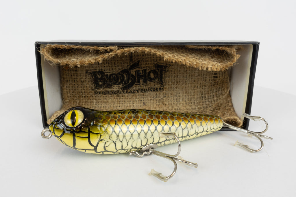 Bloodshot Raptor - Handmade Japanese Pencil Bait - Snake Skin pattern, new in original packaging, side view of fishing lure in front of packaging box. 