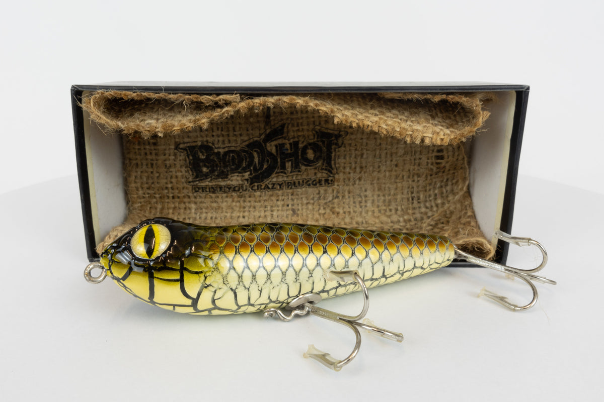 Bloodshot Raptor - Handmade Japanese Pencil Bait - Snake Skin pattern, new in original packaging, side view of fishing lure in front of packaging box. 