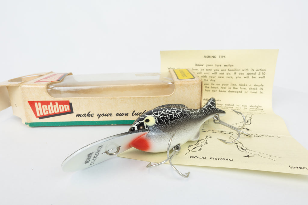 Heddon Crackleback 8000 WBC - White Black Crackle - vintage fishing lure from the USA in original packaging. View of lure in front of box and paperwork.