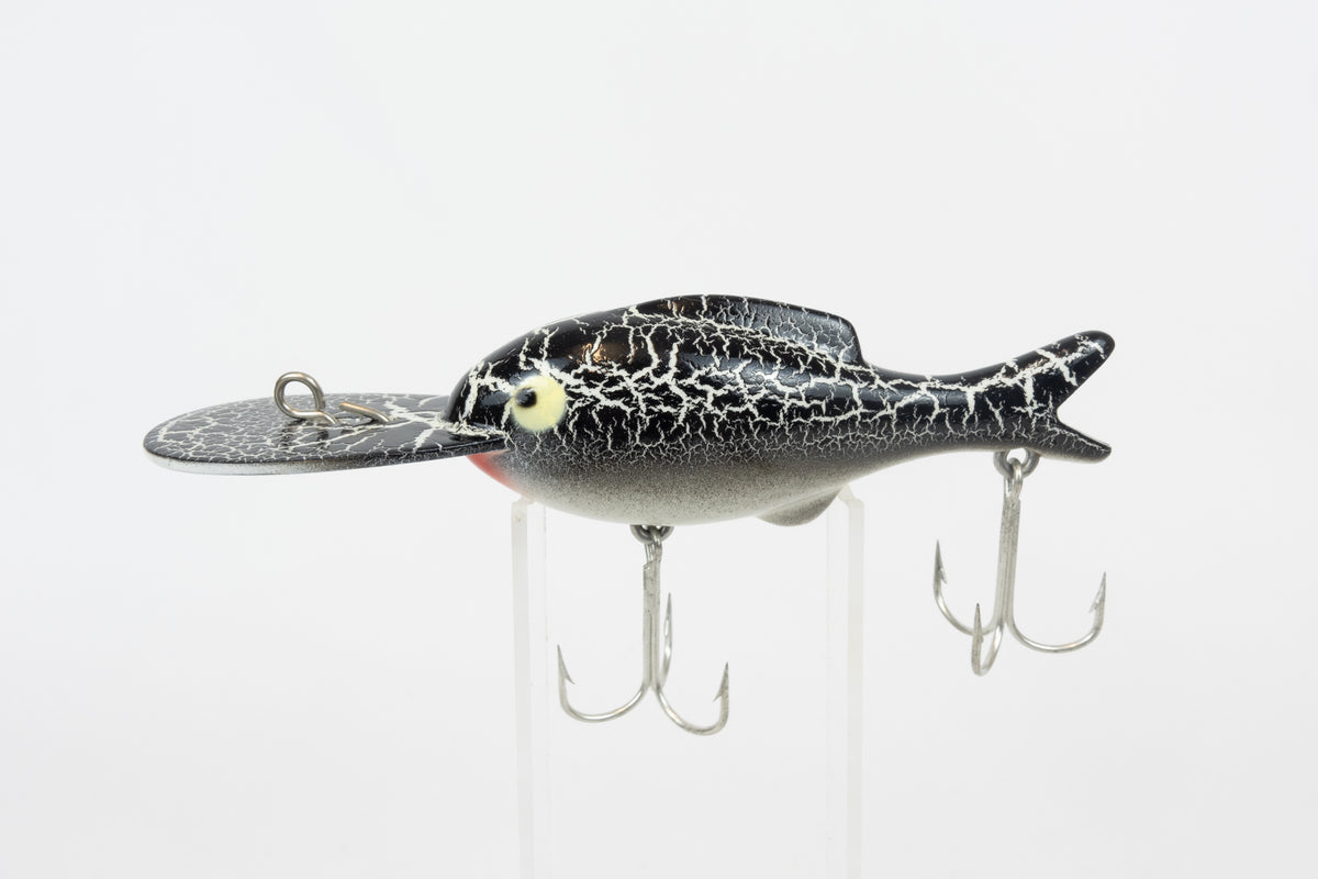Heddon Crackleback 8000 WBC - White Black Crackle - vintage fishing lure from the USA in original packaging. Left side view of lure on stand