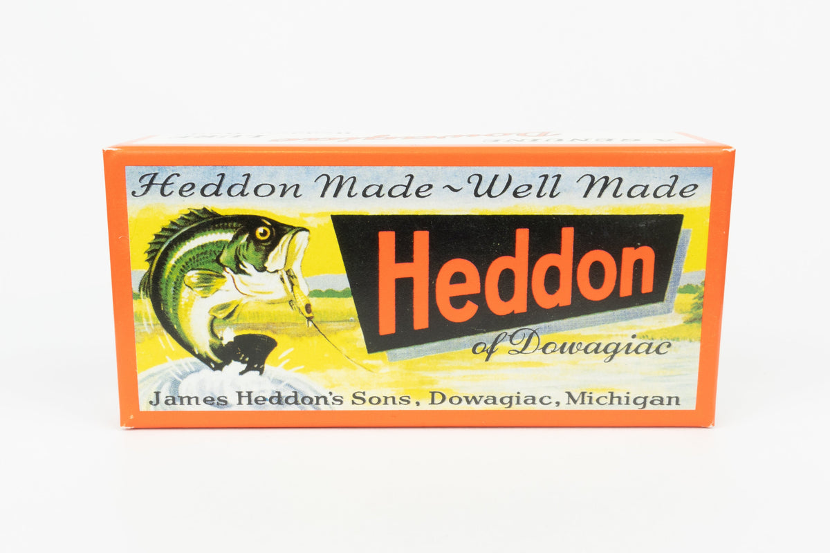A vintage-style Heddon card box featuring an orange border, a fish illustration, and the text 'Heddon Made Well Made' on a white background.